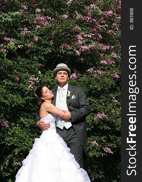 Just after the wedding, bride and groom standing in front of flowering tree in bright sunlight. Just after the wedding, bride and groom standing in front of flowering tree in bright sunlight