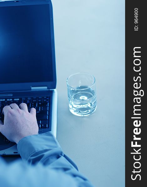 Business man in gray shirt is typing on his laptop with a glass of water next to him on the table. Business man in gray shirt is typing on his laptop with a glass of water next to him on the table