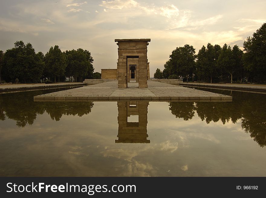 Lie-down image of a centred front perspective of the Temple of Debod in Madrid. The first arch of the monumental group is in the middle of the photo and has a line of trees at each side. The afternoon sky is the best background. A symmetry is created by the reflect of the whole enviroment in the water, that play as a mirror. Lie-down image of a centred front perspective of the Temple of Debod in Madrid. The first arch of the monumental group is in the middle of the photo and has a line of trees at each side. The afternoon sky is the best background. A symmetry is created by the reflect of the whole enviroment in the water, that play as a mirror