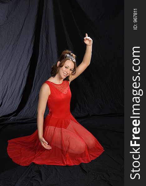 A ballerina in a red dress posed facing the camera with left arm raised.  Kneeling. A ballerina in a red dress posed facing the camera with left arm raised.  Kneeling