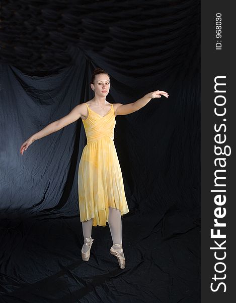 A ballerina poses on pointe in yellow lyrical costume