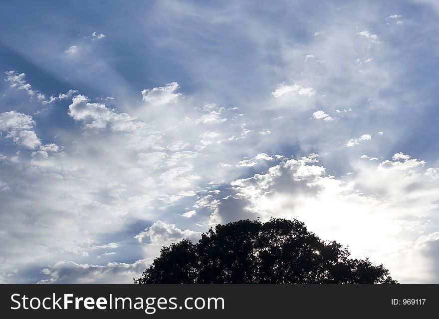 Sun rays coming off clouds in a beautiful blue sky.