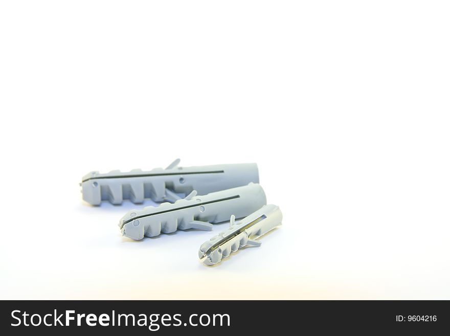 Three grey plastic wall plugs lying down on a white background. Three grey plastic wall plugs lying down on a white background