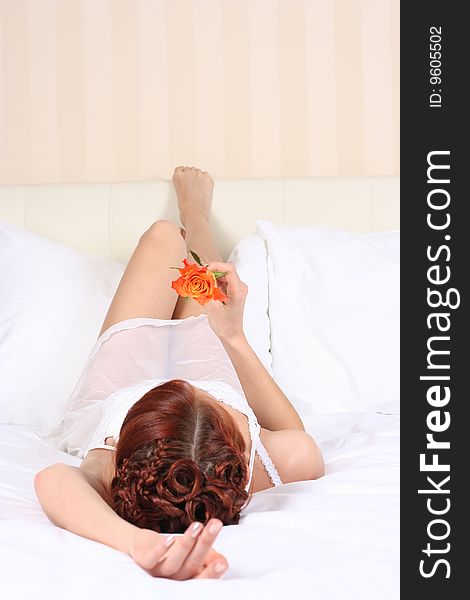 Young woman in bed with orange rose (rose in focus)