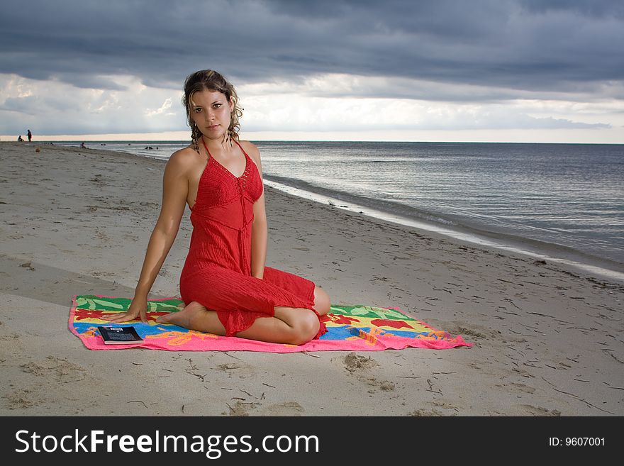 Girl with red dress on a towel, in the beach