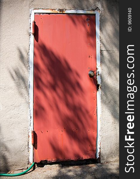 Old red door with a green rubber hose coming at the bottom