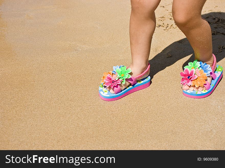 Legs of a two years old child girl on the sand, wearing a pair of a lovely flower decorated flip flops. Beach, summer, fun, vacation concept. Space for copy. Jpeg with clipping path included. Legs of a two years old child girl on the sand, wearing a pair of a lovely flower decorated flip flops. Beach, summer, fun, vacation concept. Space for copy. Jpeg with clipping path included.