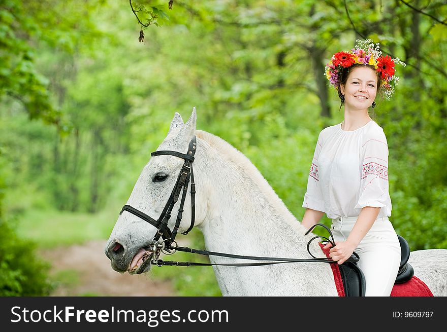 Smiling girl in floral wreath riding horse