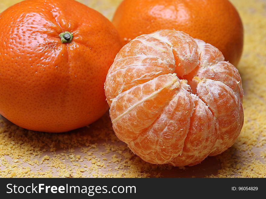 A peeled mandarin next to a couple of unpeeled ones.