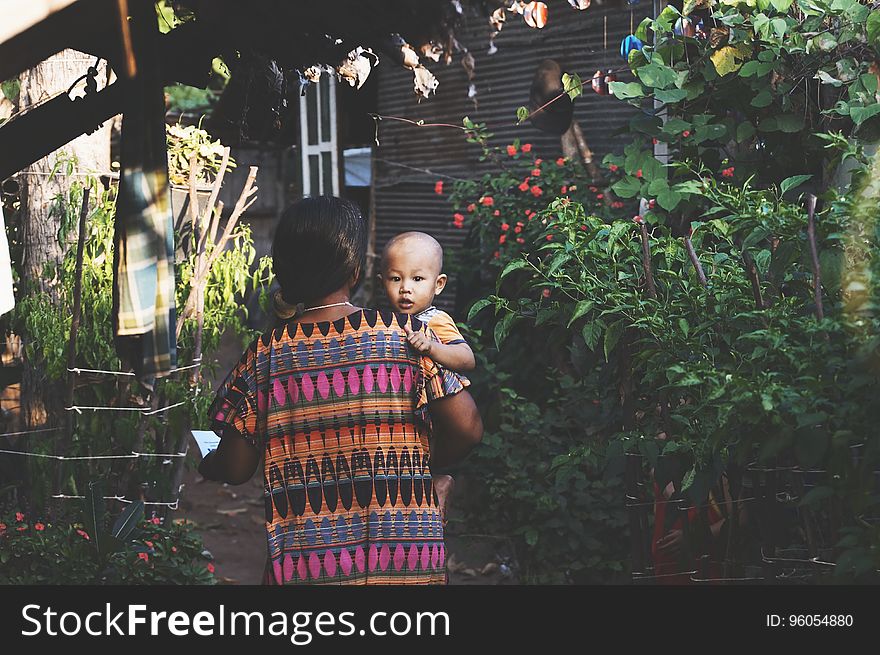 Woman in Orange Pink Aztec Dress Carrying Child in Orange Shirt