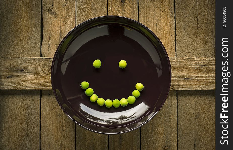 Beans in shape of smiling face on brown plate on rustic wooden table. Beans in shape of smiling face on brown plate on rustic wooden table.