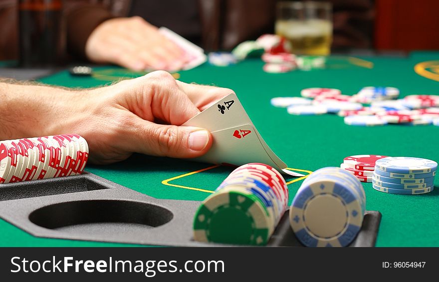 A person looking at their hand with two aces at a poker game.