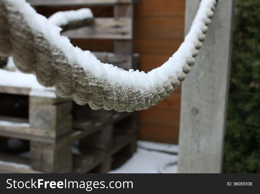 A heavy duty rope covered in snow hanging from posts in the garden and behind it a pile of (blurred) wooden pallets. A heavy duty rope covered in snow hanging from posts in the garden and behind it a pile of (blurred) wooden pallets.