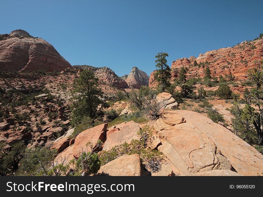 Red sandstone, rocks, sand and scrub making a barren desert landscape with red cliffs, blue cloudless sky. Red sandstone, rocks, sand and scrub making a barren desert landscape with red cliffs, blue cloudless sky.