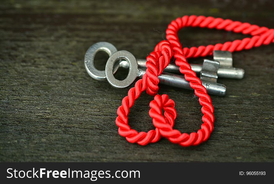 Close up of red nylon rope over silver keys on rustic wooden table. Close up of red nylon rope over silver keys on rustic wooden table.
