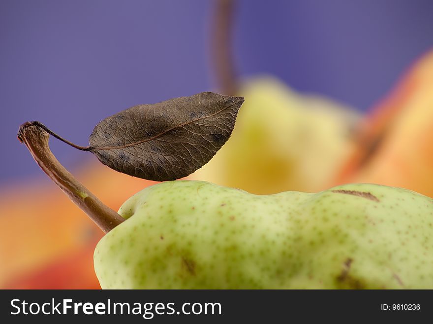 Pear part with leaflet on blue background with an red apple out of focus. Focus limited. Pear part with leaflet on blue background with an red apple out of focus. Focus limited.