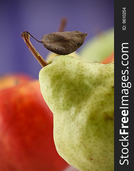 Pear part with leaflet on blue background with an red apple out of focus. Focus limited. Pear part with leaflet on blue background with an red apple out of focus. Focus limited.