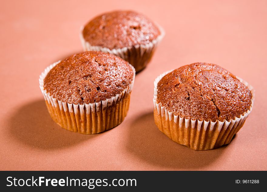 Three chocolate muffins on brown background