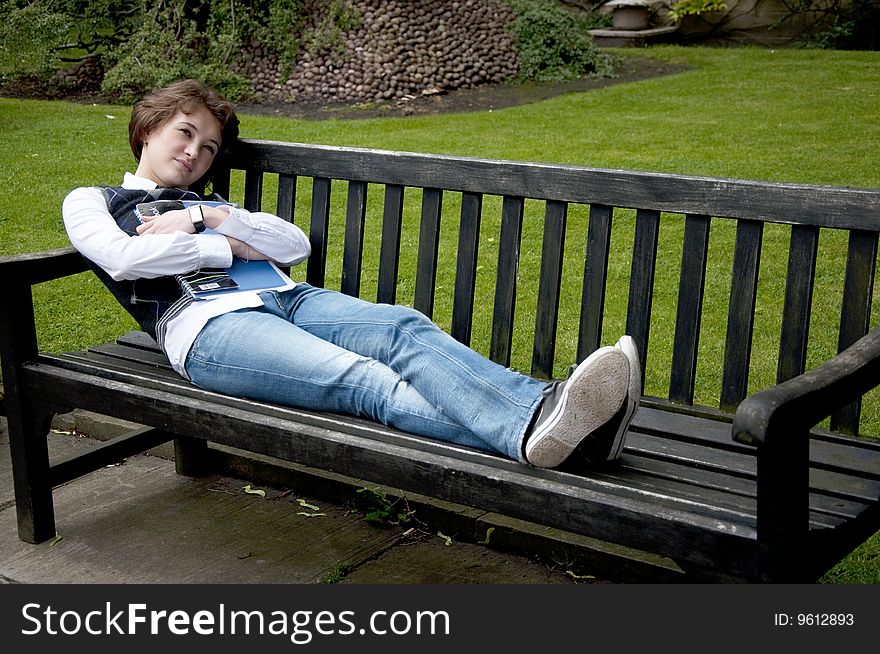 Young student woman lays on the bench with a writing-book and dreaming about her exams succeed. Young student woman lays on the bench with a writing-book and dreaming about her exams succeed
