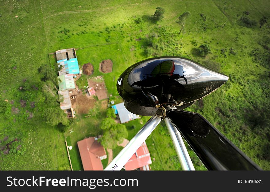 An aerial view from the seat of a microlite. you can see the wheel and the reflection of the light aircraft against the sky behind it. the lush green landscape below is dotted with small buildings. An aerial view from the seat of a microlite. you can see the wheel and the reflection of the light aircraft against the sky behind it. the lush green landscape below is dotted with small buildings.