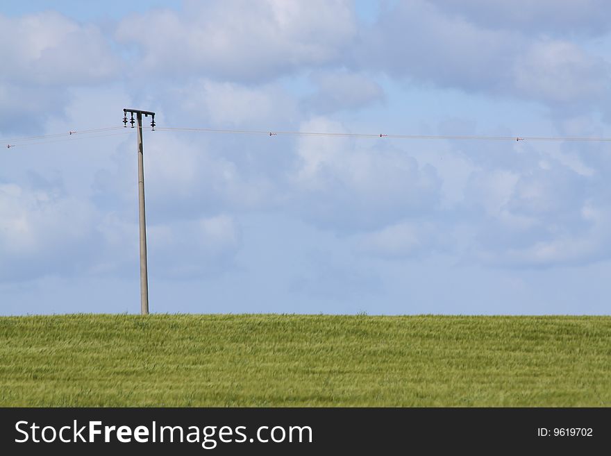 An electricity post  standing alone in a wide landscape against a blue cloudy sky. An electricity post  standing alone in a wide landscape against a blue cloudy sky