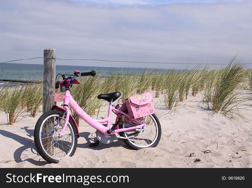 Childrens bike in the dunes, parked against a pole with view on the sea