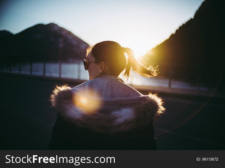 A girl on a viewpoint looking at sun setting between mountains. A girl on a viewpoint looking at sun setting between mountains.