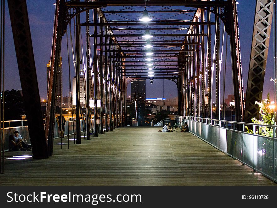 Couple sitting on illuminated bridge in city at night.