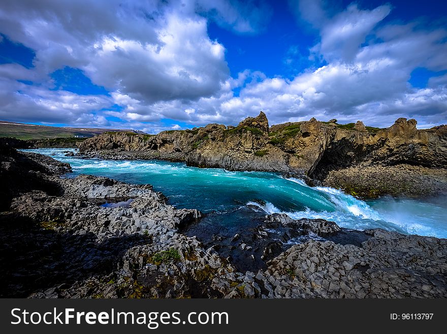 River with rocky shores in countryside against blue skies on sunny day.