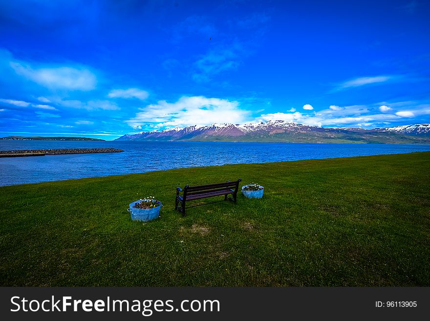A bench by the shore with a mountain range in the distance. A bench by the shore with a mountain range in the distance.