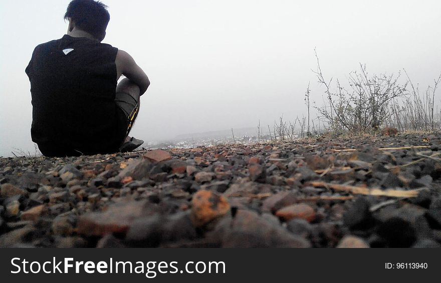 A man sitting on gravel with mist in the distance.