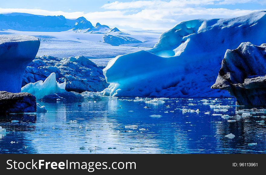 Icebergs floating in water along edge of glacier on sunny day. Icebergs floating in water along edge of glacier on sunny day.