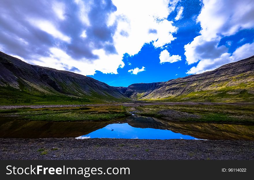 Blue skies reflecting in lake in field of mountain valley countryside on sunny day.