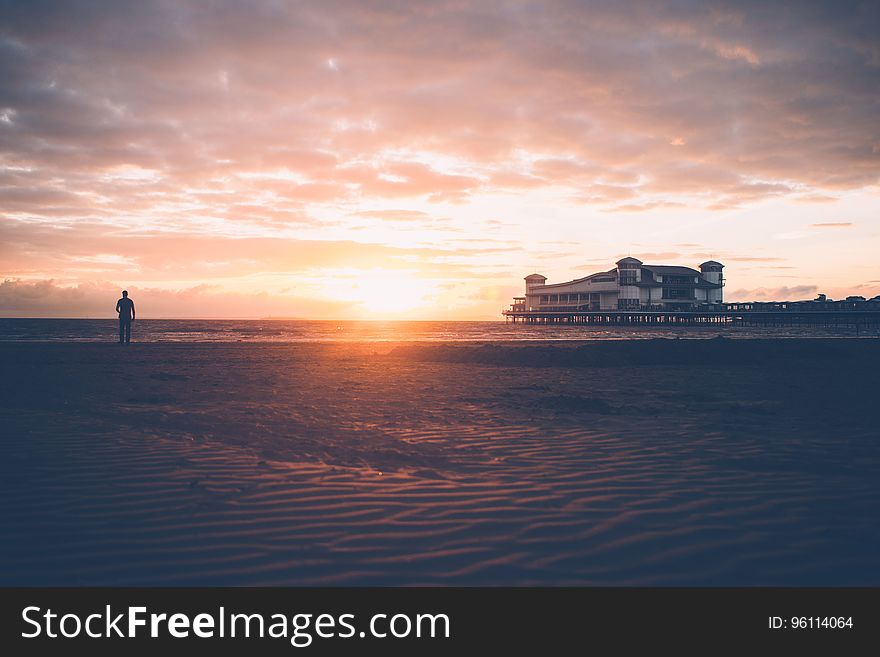 A sunset on a beach with a person looking at the sea. A sunset on a beach with a person looking at the sea.