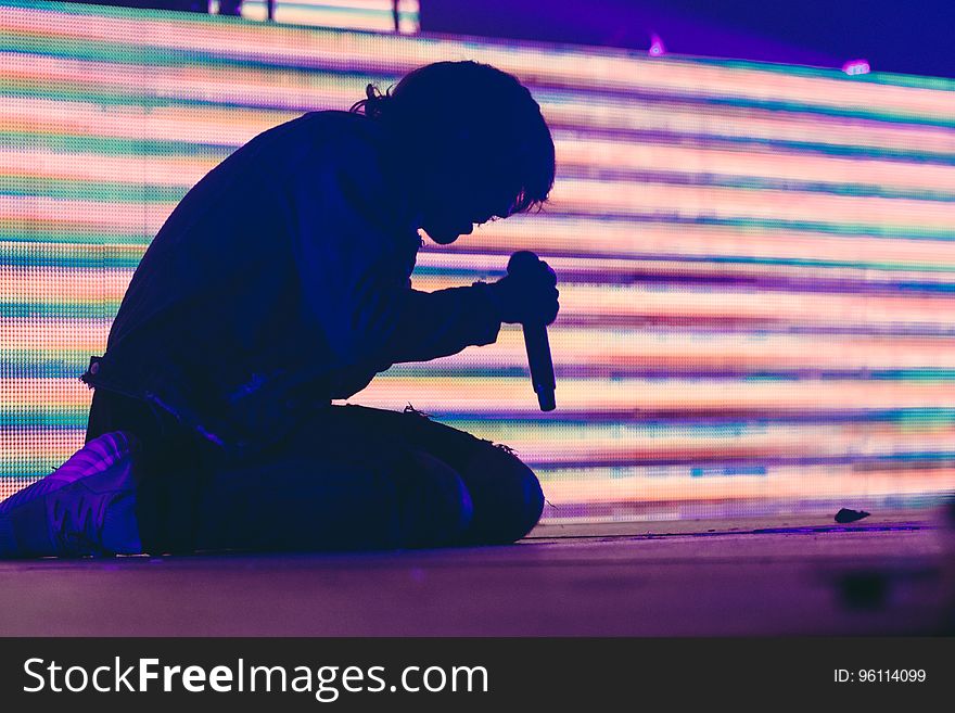 Side view of silhouetted person singing with microphone bright corrugated effect background.