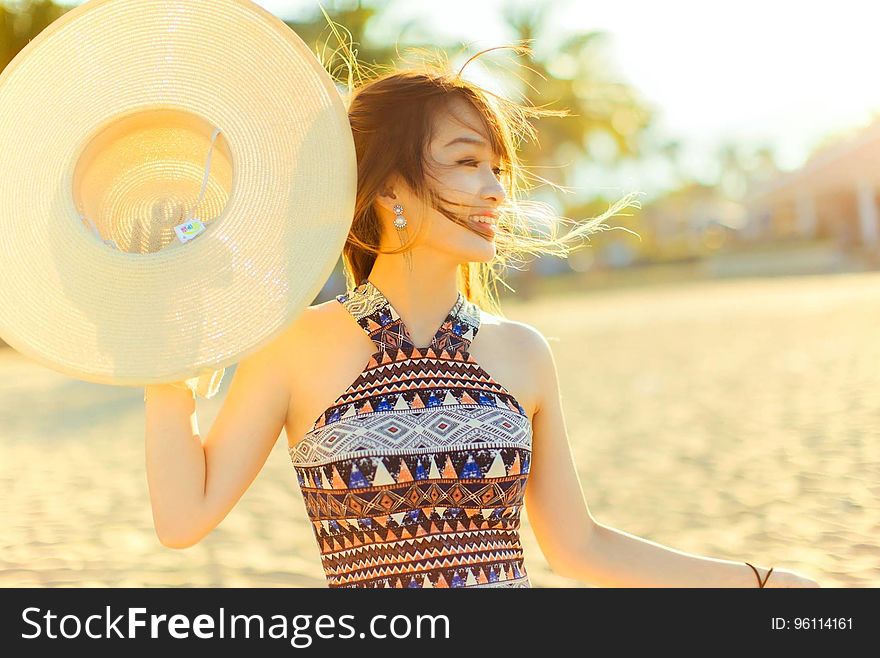 A portrait of a young smiling woman on a beach holding a hat. A portrait of a young smiling woman on a beach holding a hat.