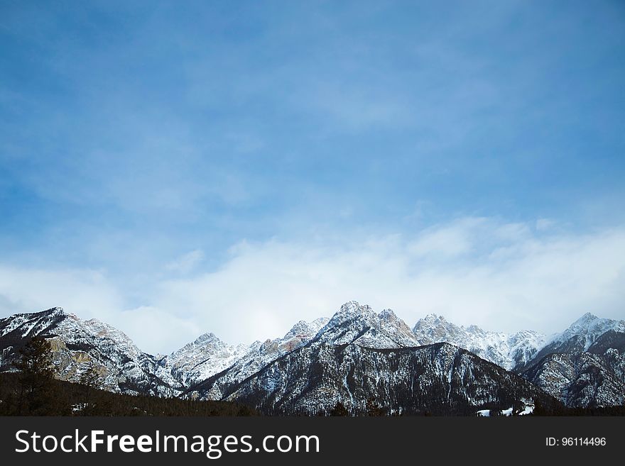 Scenic view of snow capped mountain range with blue sky and cloudscape background.