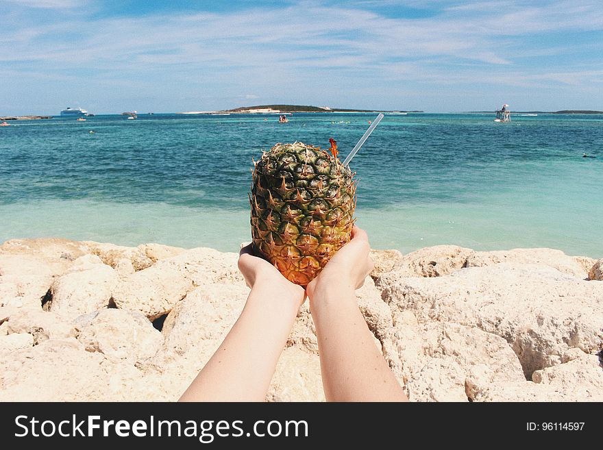 A person holding a tropical drink on a beach. A person holding a tropical drink on a beach.