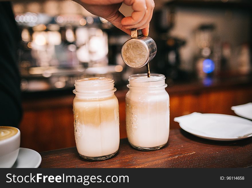 Barista making coffee and cream drinks in glass jars on wooden countertop. Barista making coffee and cream drinks in glass jars on wooden countertop.