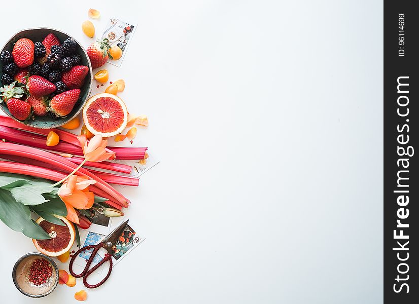 Border of fresh ripe berries, rhubarb, oranges, flowers, seed and scissors on white with copy space. Border of fresh ripe berries, rhubarb, oranges, flowers, seed and scissors on white with copy space.