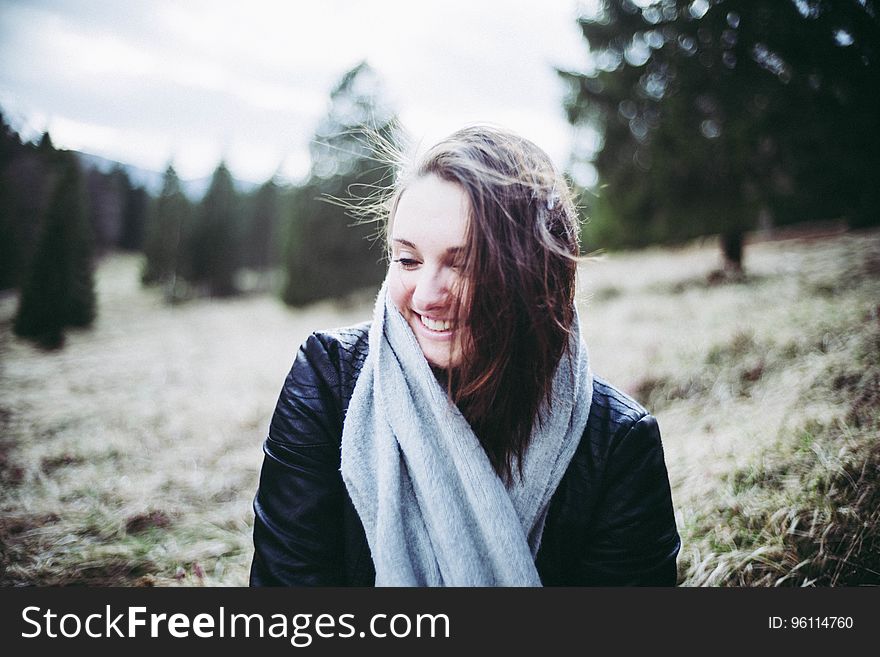 Portrait of smiling woman wearing fall jacket and scarf standing in field of sunny forest. Portrait of smiling woman wearing fall jacket and scarf standing in field of sunny forest.