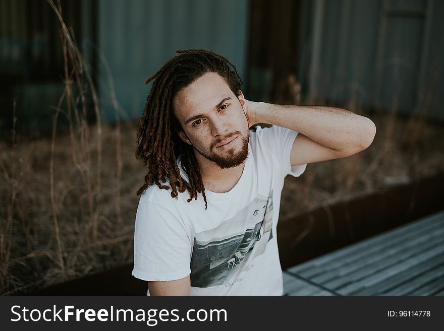 Portrait of man with cornrow braids sitting outdoors on sunny day. Portrait of man with cornrow braids sitting outdoors on sunny day.