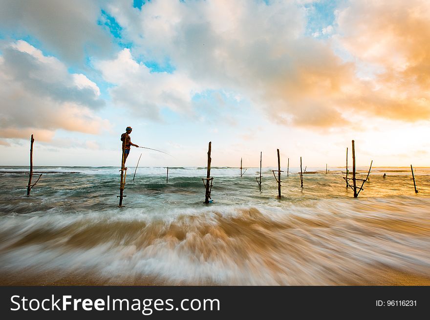 Man Standing in Wood in the Middle of the Ocean While Fishing Under Blue and White Sky during Day Time