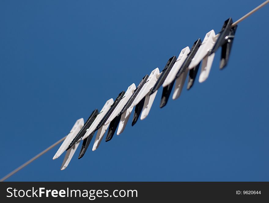 A row of black and white clothes pegs on a line with a blue sky background
