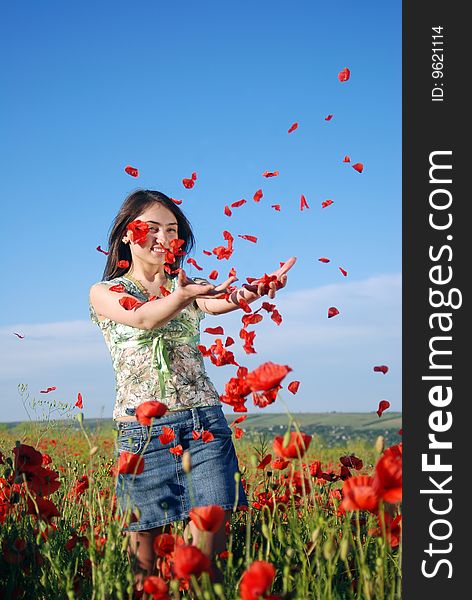 A beautiful girl standing on a field filled with red poppies and catches falling poppie petals. A beautiful girl standing on a field filled with red poppies and catches falling poppie petals