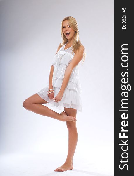 A young beautiful blonde in a white dress standing barefoot. A young beautiful blonde in a white dress standing barefoot