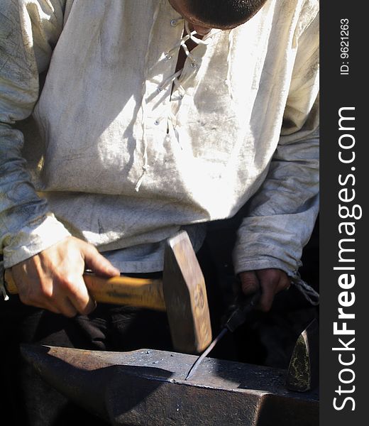 A young blacksmith in white shirt forging a nail. A young blacksmith in white shirt forging a nail