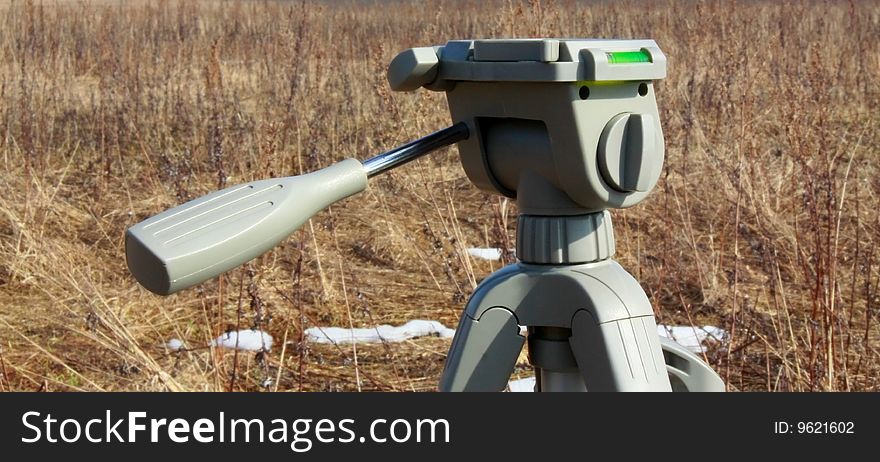 Tripod head in field with melting snow.