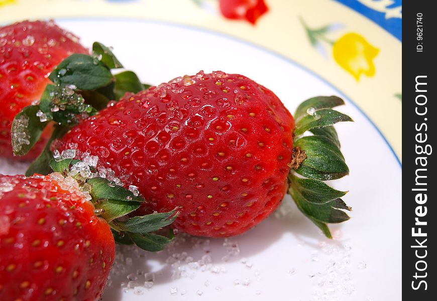 Three fresh ripe strawberries sprinkled with course white sugar on colorful flower pattern decorated dish. Three fresh ripe strawberries sprinkled with course white sugar on colorful flower pattern decorated dish.