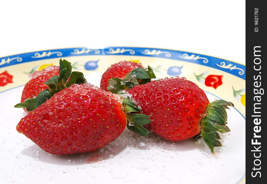 Front view of four fresh ripe strawberries sprinkled with course white sugar on colorful flower pattern decorated dish. Front view of four fresh ripe strawberries sprinkled with course white sugar on colorful flower pattern decorated dish.